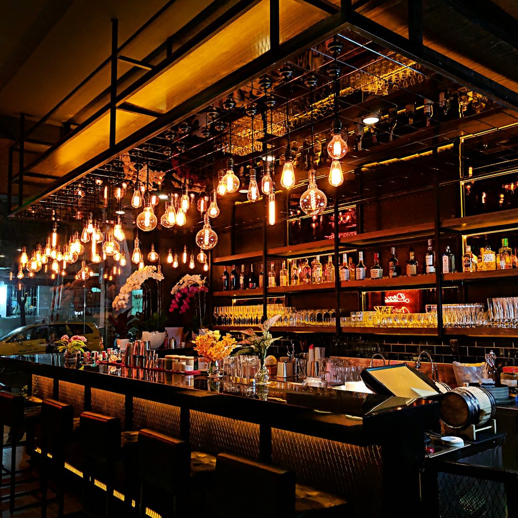 Warmly lit craft bar with edison bulbs and bottles, the kind of local venue that hosts plant bingo nights